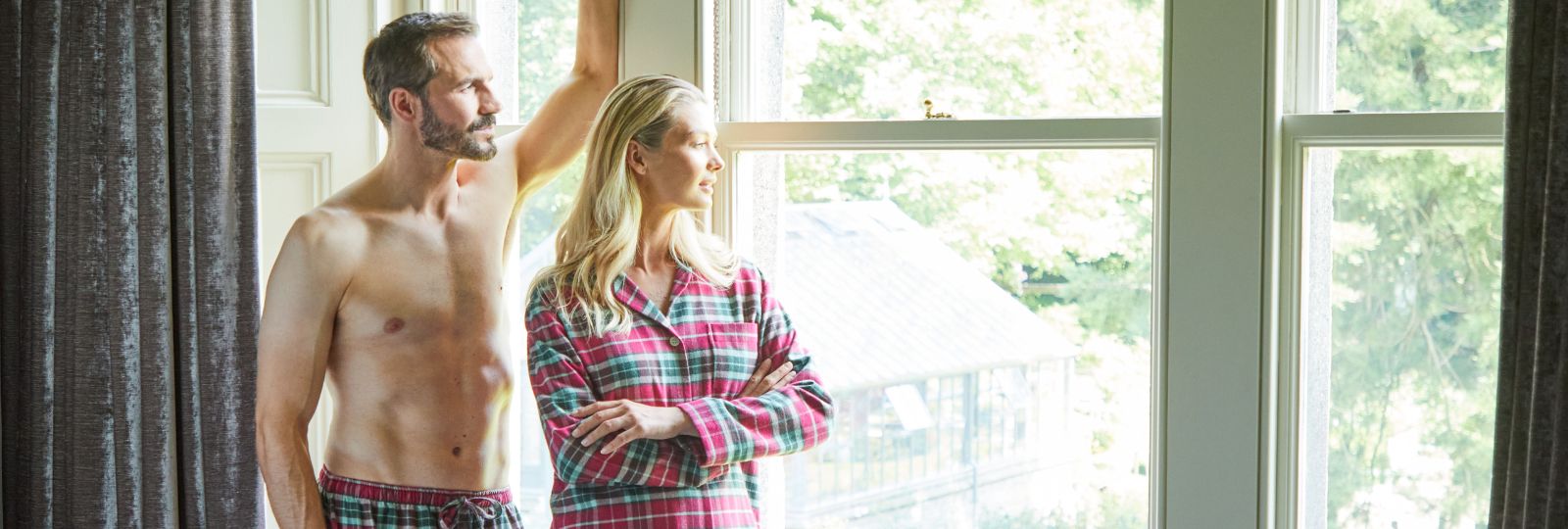 British Boxers loungewear, a couple in tartan pyjamas by a bright sash window